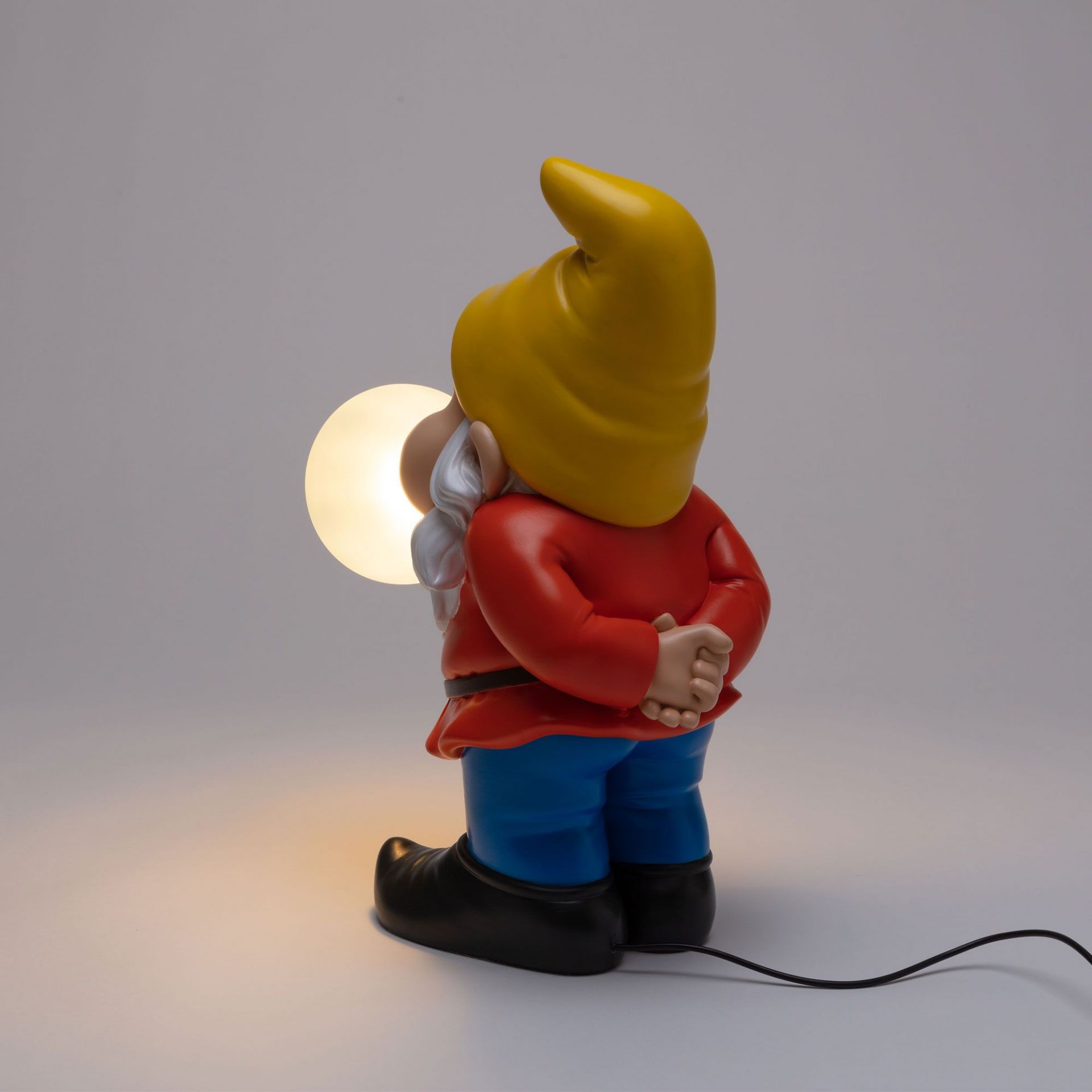 Rückansicht der Seletti Gummy Snooping Lampe: Gartenzwerg mit gelber Mütze und leuchtender Kugel.
