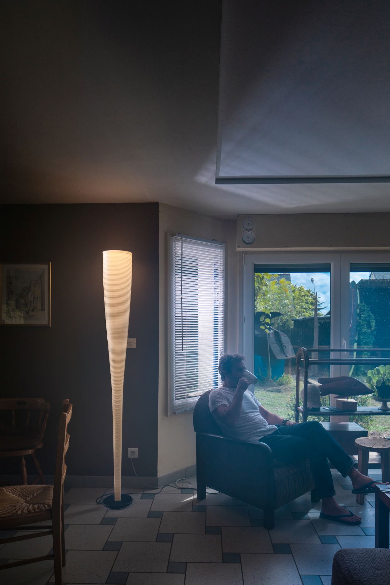 Mite LED Stehleuchte von Foscarini im Wohnzimmer, neben einem Mann im Sessel.