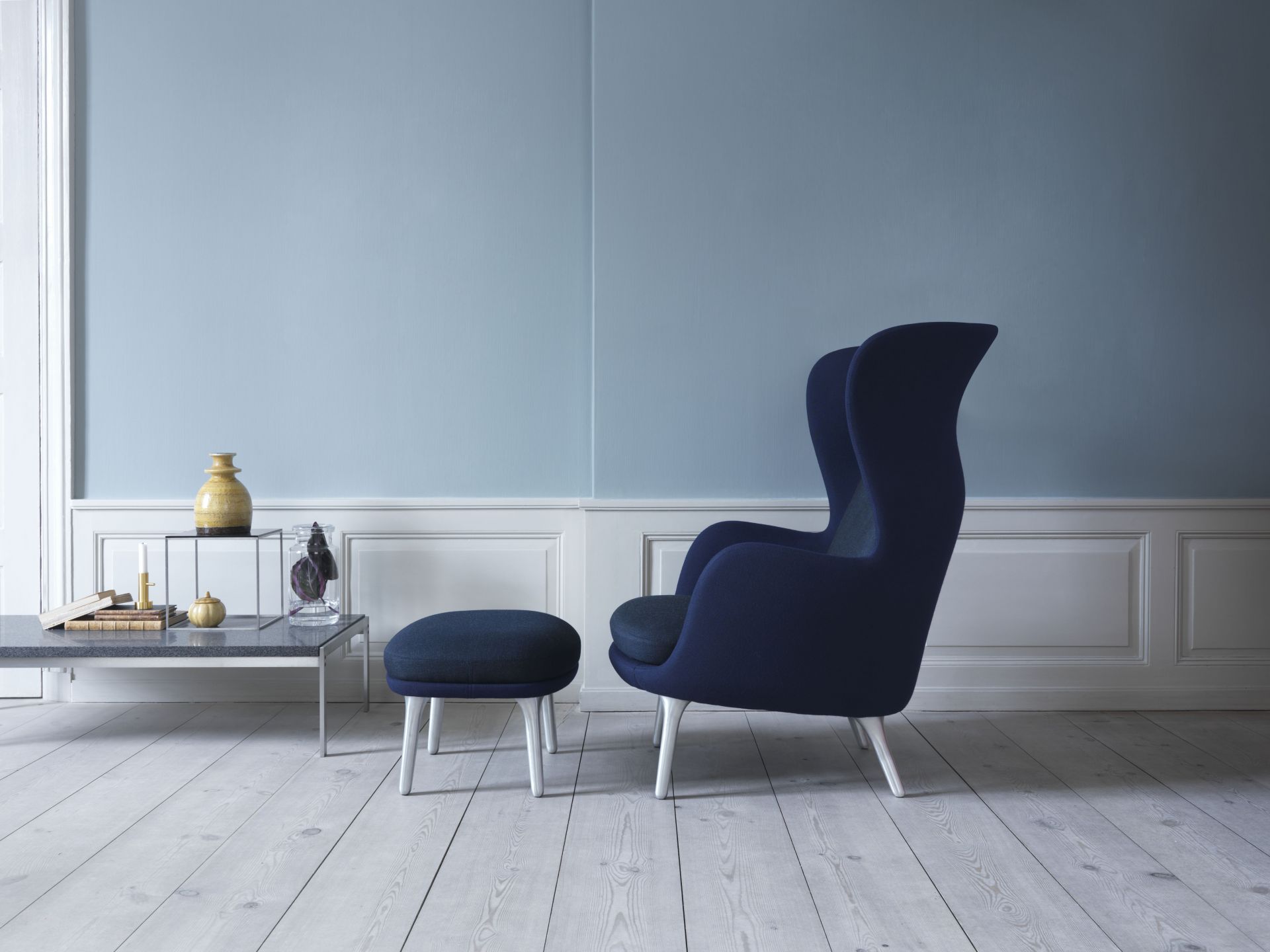 Blauer Ro Sessel von Fritz Hansen mit passendem Hocker auf hellem Holzboden in minimalistischem Ambiente.