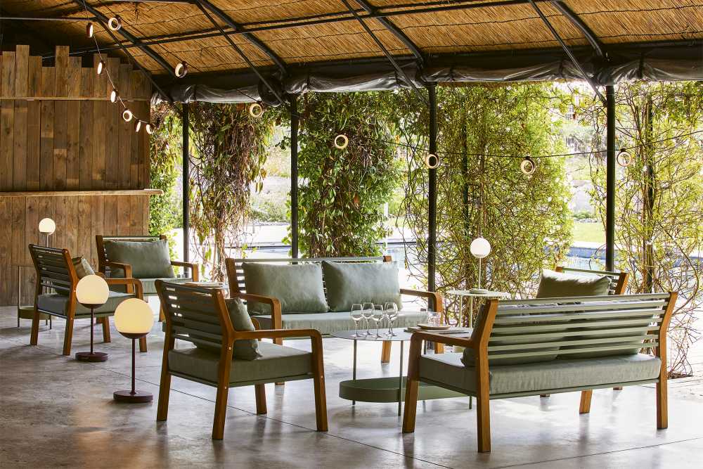 Somerset 2-Sitzer Outdoor Sofa von Fermob in grüner Lounge-Atmosphäre mit passenden Sesseln und Tisch.