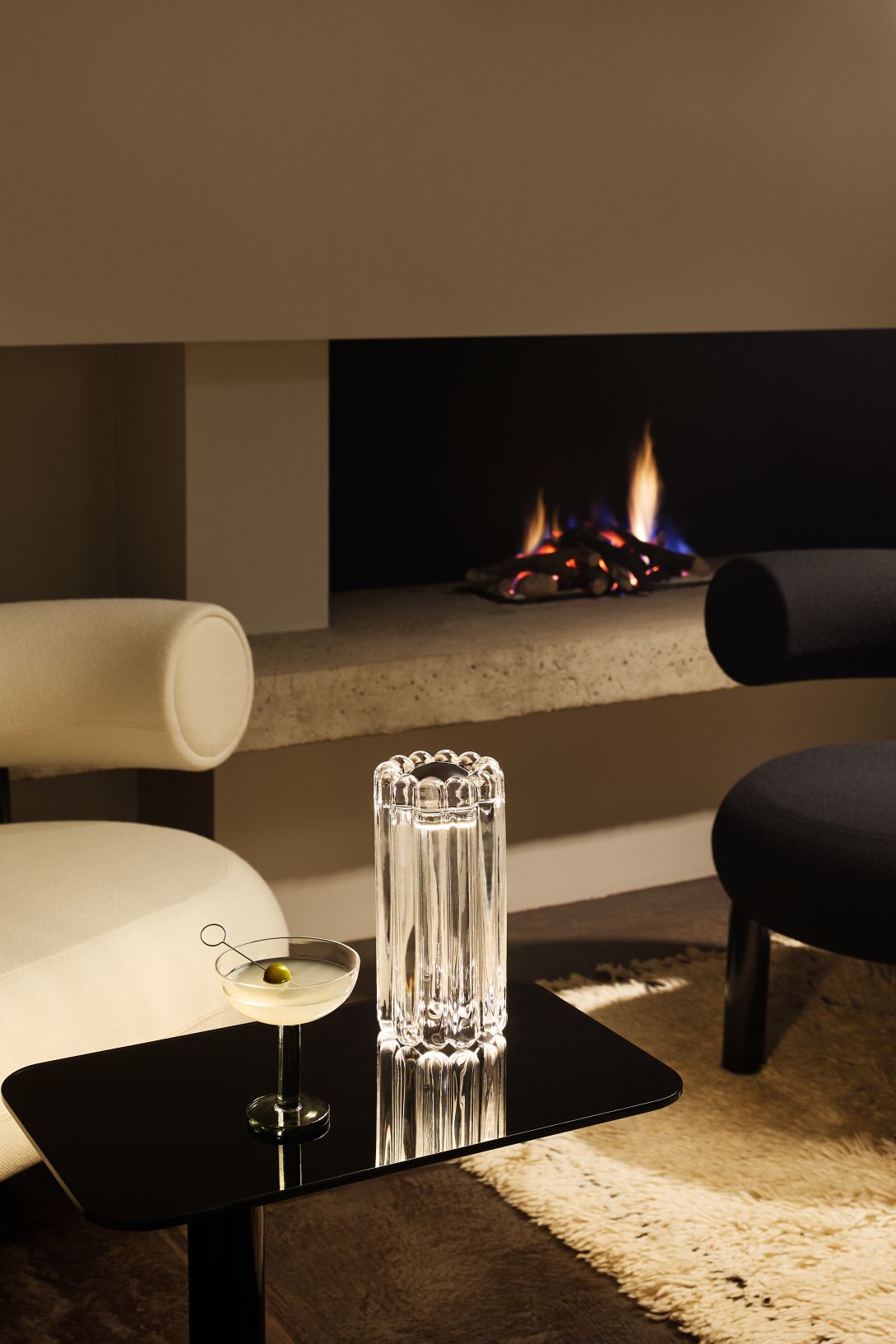 Nahaufnahme der Tom Dixon Press Tischleuchte aus Glas auf schwarzem Tisch mit Cocktail und Kamin.