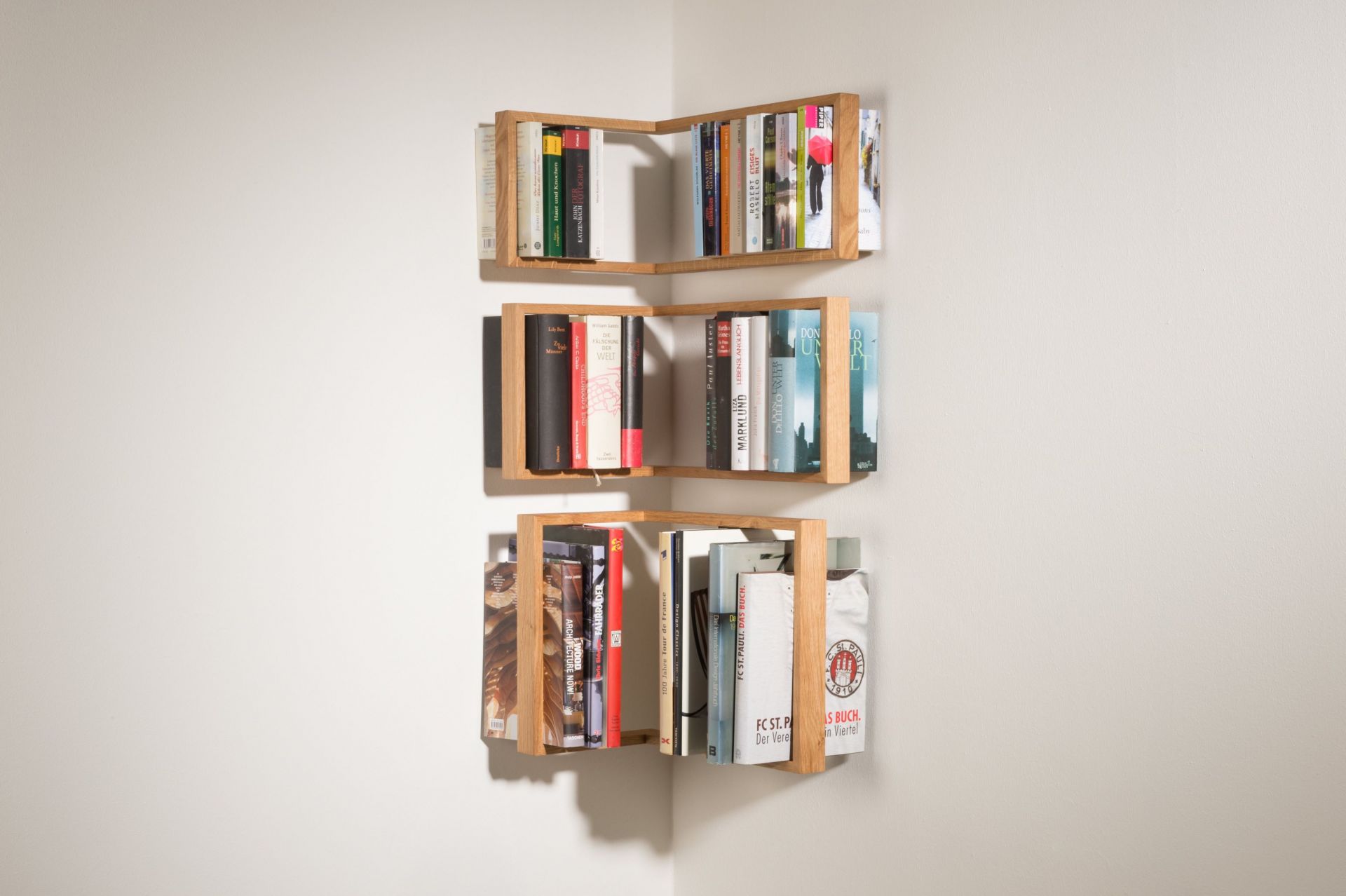 Eiche Regal b-eck, das kleine b, dreifach übereinander an einer weißen Ecke montiert und mit Büchern gefüllt.
