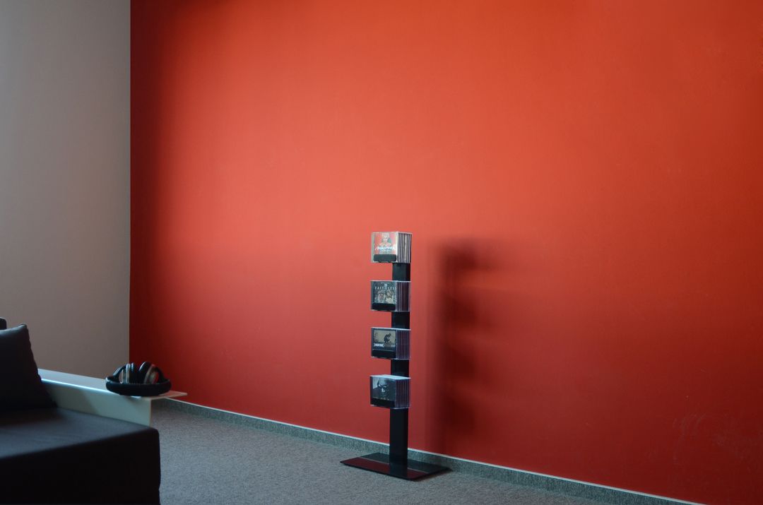 Schwarzes CD-Baum Einzeln Standregal mit CDs vor roter Wand. CD-Regal für Musiksammlung.