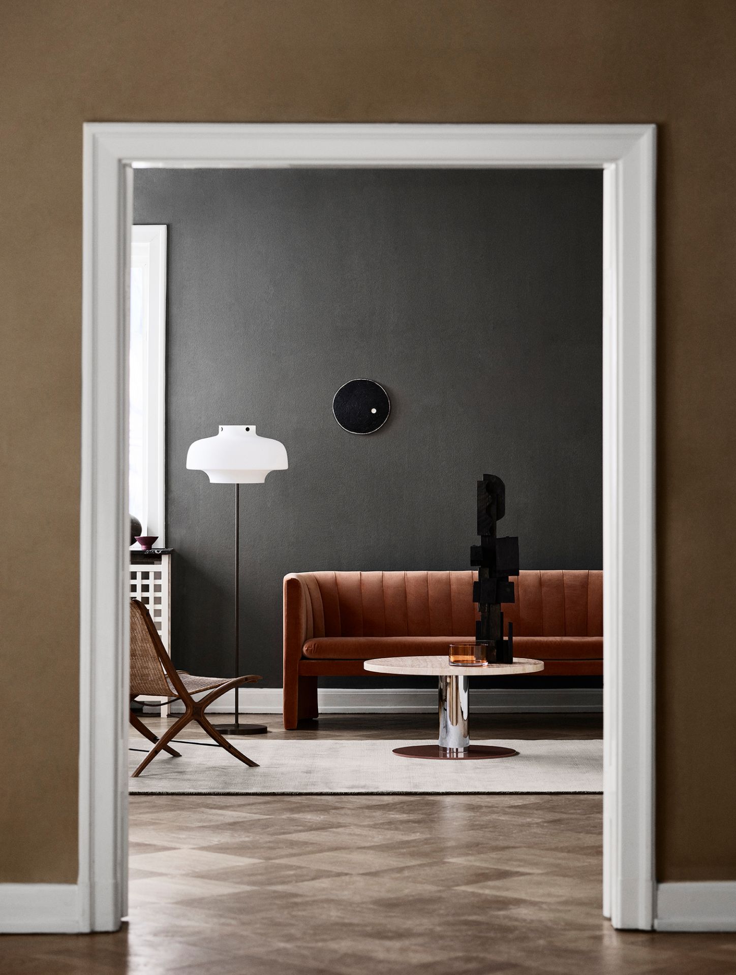 Wohnzimmer mit braunem Loafer Sofa von AndTradition, Tisch, Lampe und Stuhl durch Türrahmen.