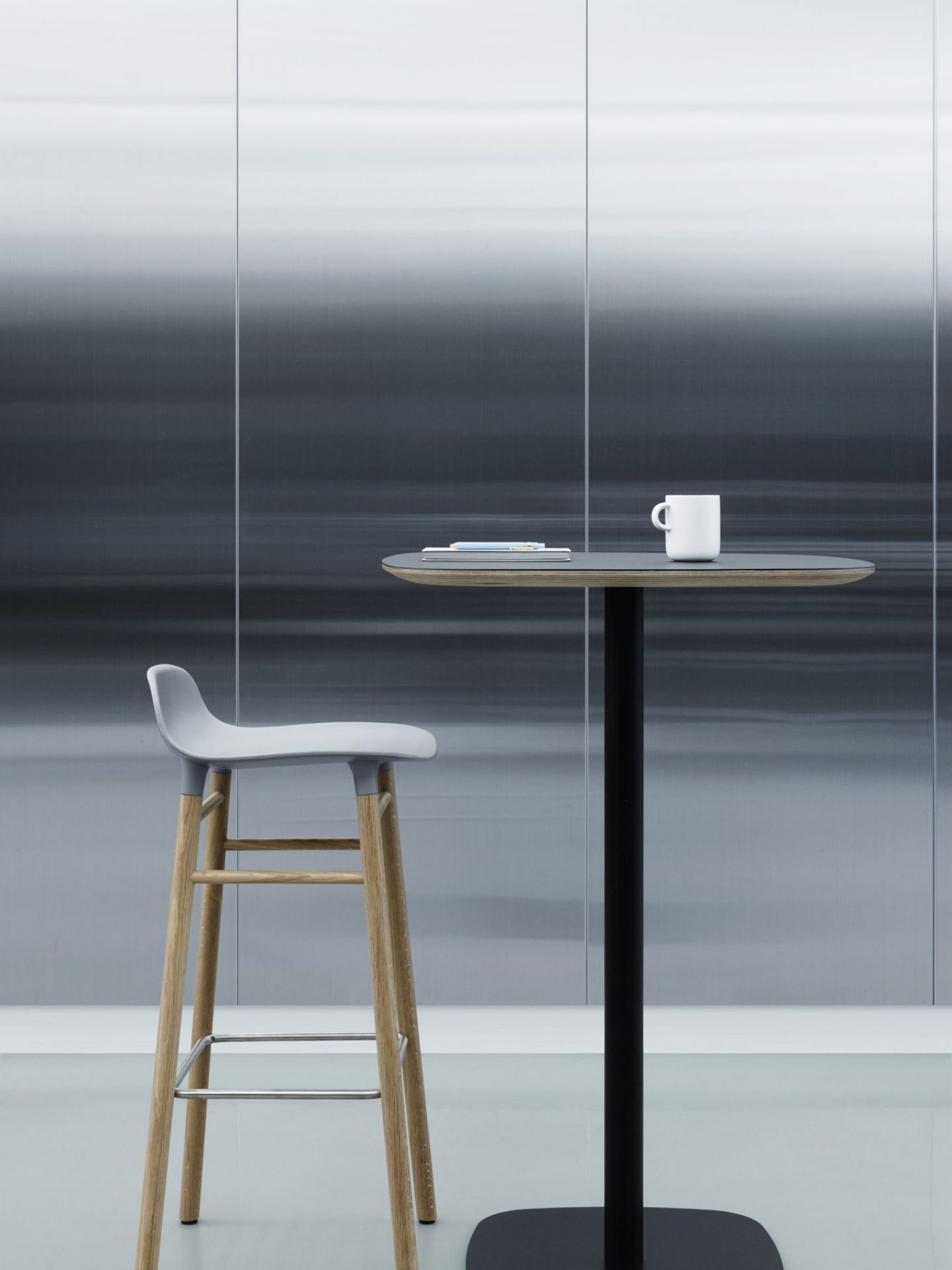 Normann Copenhagen Form Barhocker H 75 cm aus Holz in Grau neben Stehtisch mit Tasse.