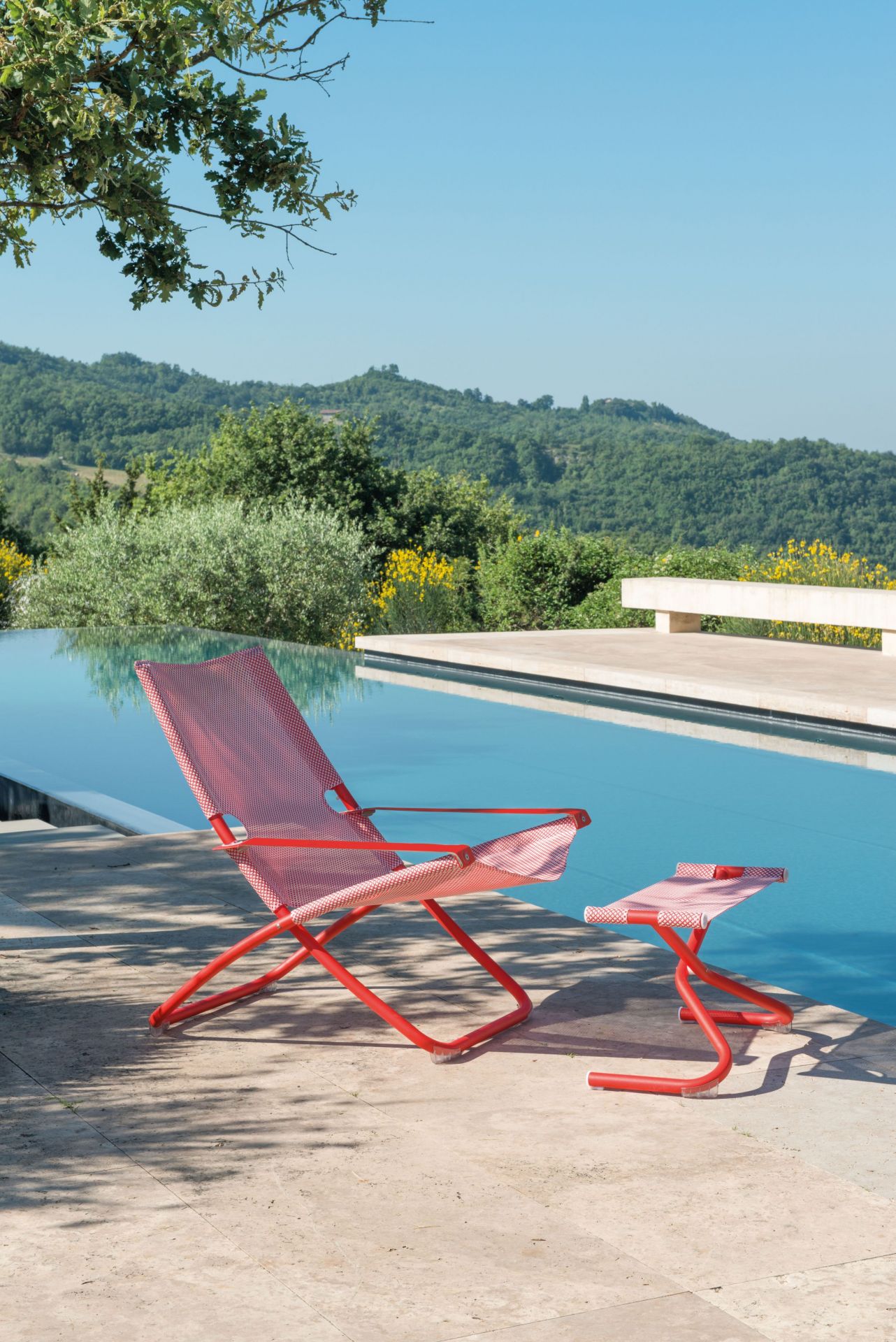 Snooze Liegestuhl am Pool: Roter Gartenstuhl mit beige-karierter Bespannung und passendem Beistelltisch.
