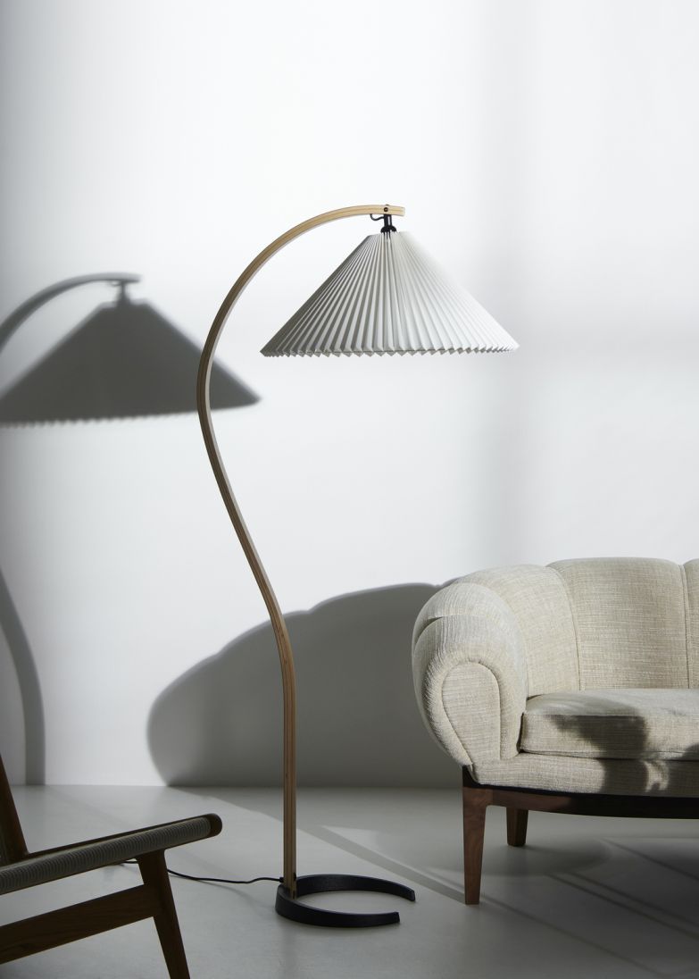 Elegante Timberline Stehleuchte von Gubi mit plissiertem Lampenschirm und gebogenem Holzfuß neben beigem Sessel.