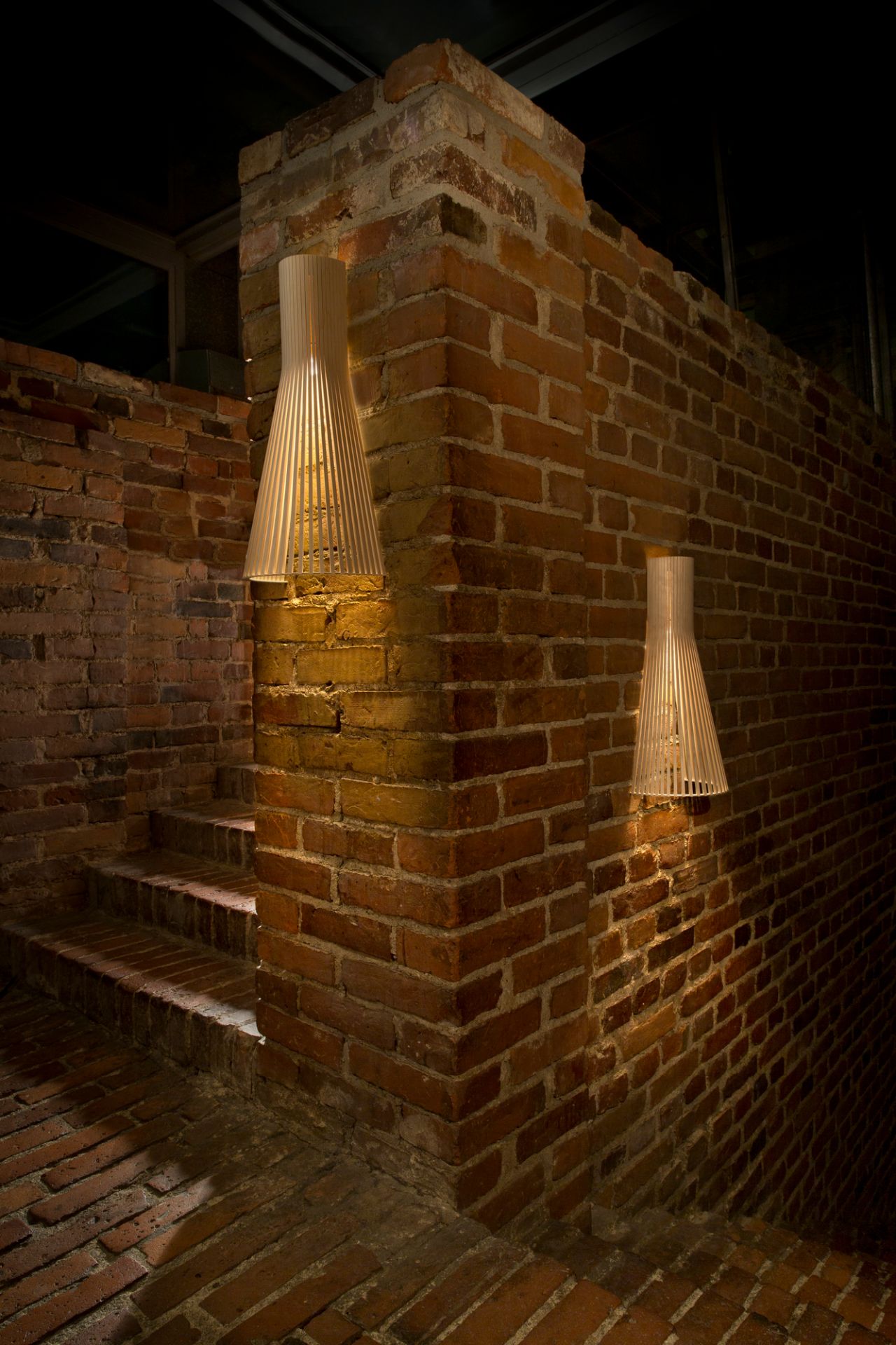 Secto Design 4230 LED Wandleuchte aus Birkenholz an einer Backsteinwand mit Treppe.
