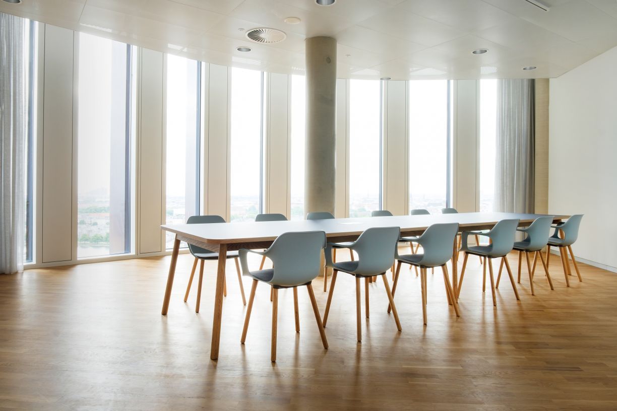 Helle Büroumgebung mit langem Tisch und mehreren grauen Vitra Hal RE Wood Stühlen.