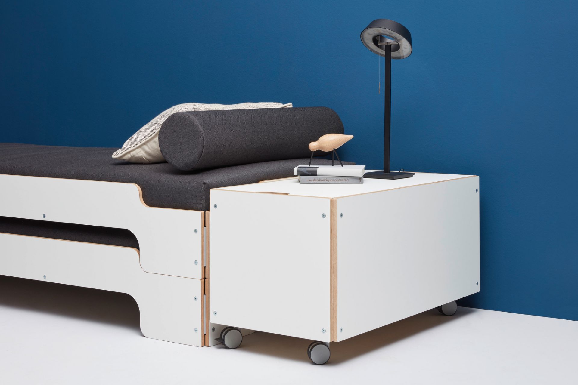 Weißer Bettkasten auf Rollen von Müller Möbelwerkstätten mit Bett, Lampe und Deko.