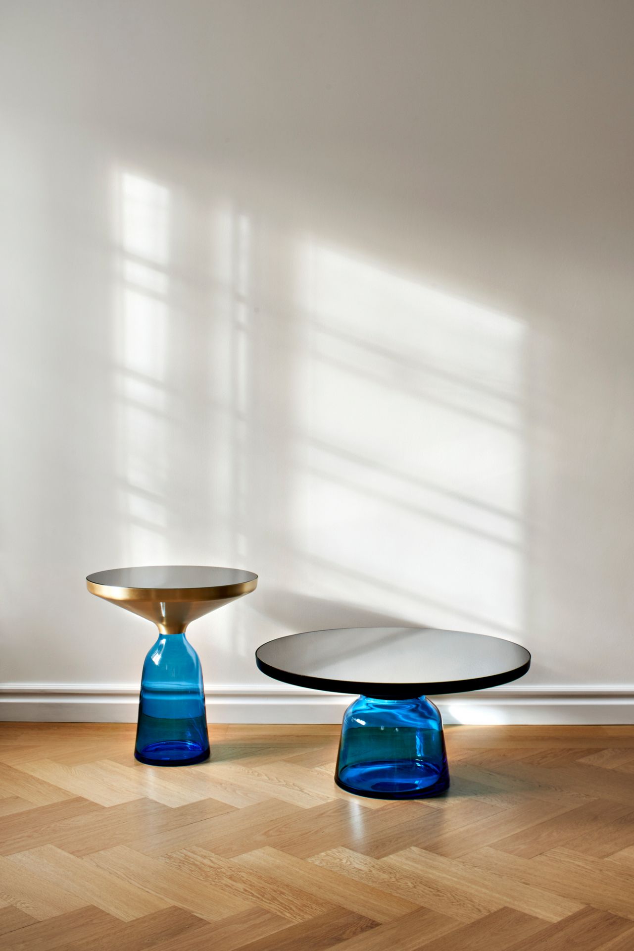 Zwei Bell Side Table Beistelltische von ClassiCon: Einer mit Messingfuß, einer mit schwarzem Fuß, beide mit blauen Glasfüßen.