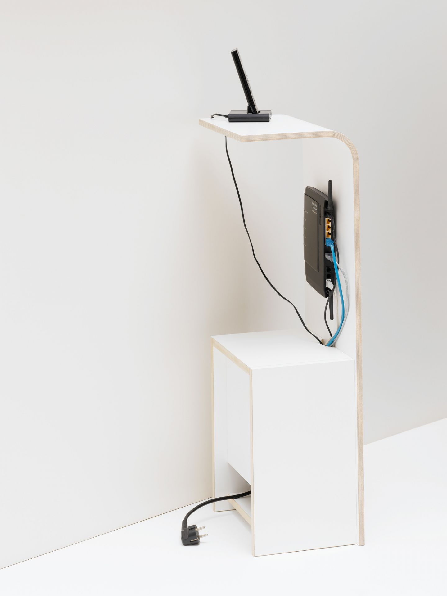 Weißes Fon Regal von Tojo mit Telefon, Router und Kabeln in minimalistischer Einrichtung.