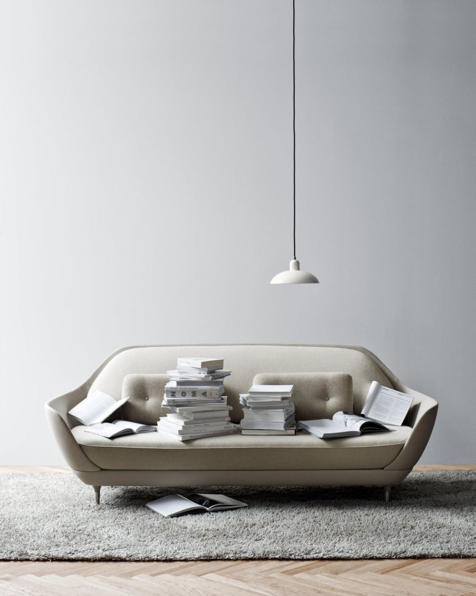 Beiges Favn Sofa von Fritz Hansen mit Bücherstapeln und offener Lampe im minimalistischen Wohnzimmer.
