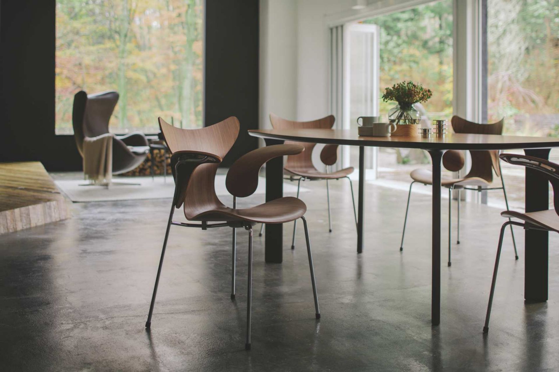 Fritz Hansen Lily Armlehnenstuhl 3208 aus Holz mit Stahlbeinen am Esstisch im modernen Wohnzimmer.