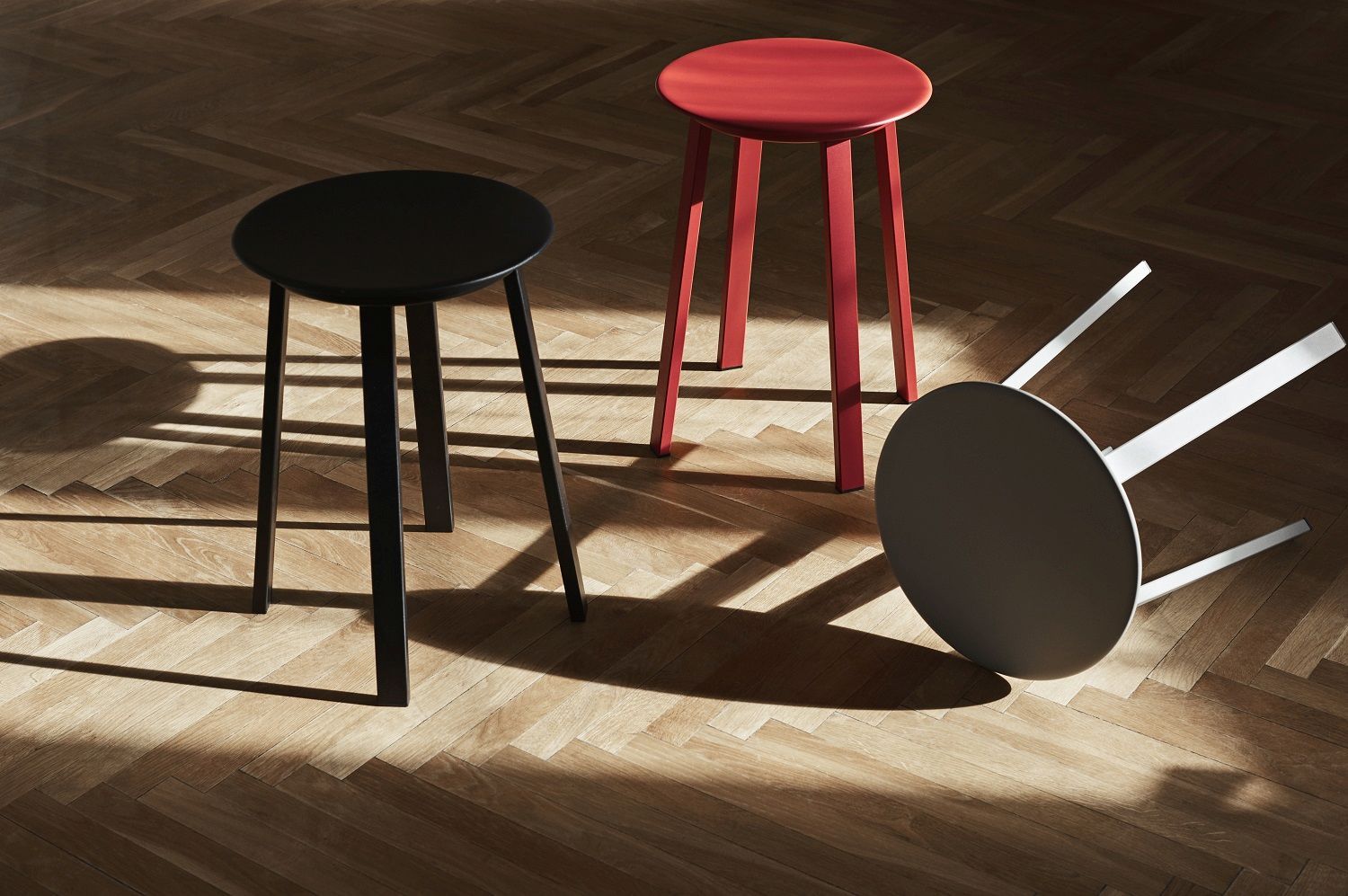 Drei Hay Revolver Stool Hocker in Schwarz, Rot und Weiß auf einem Holzboden.