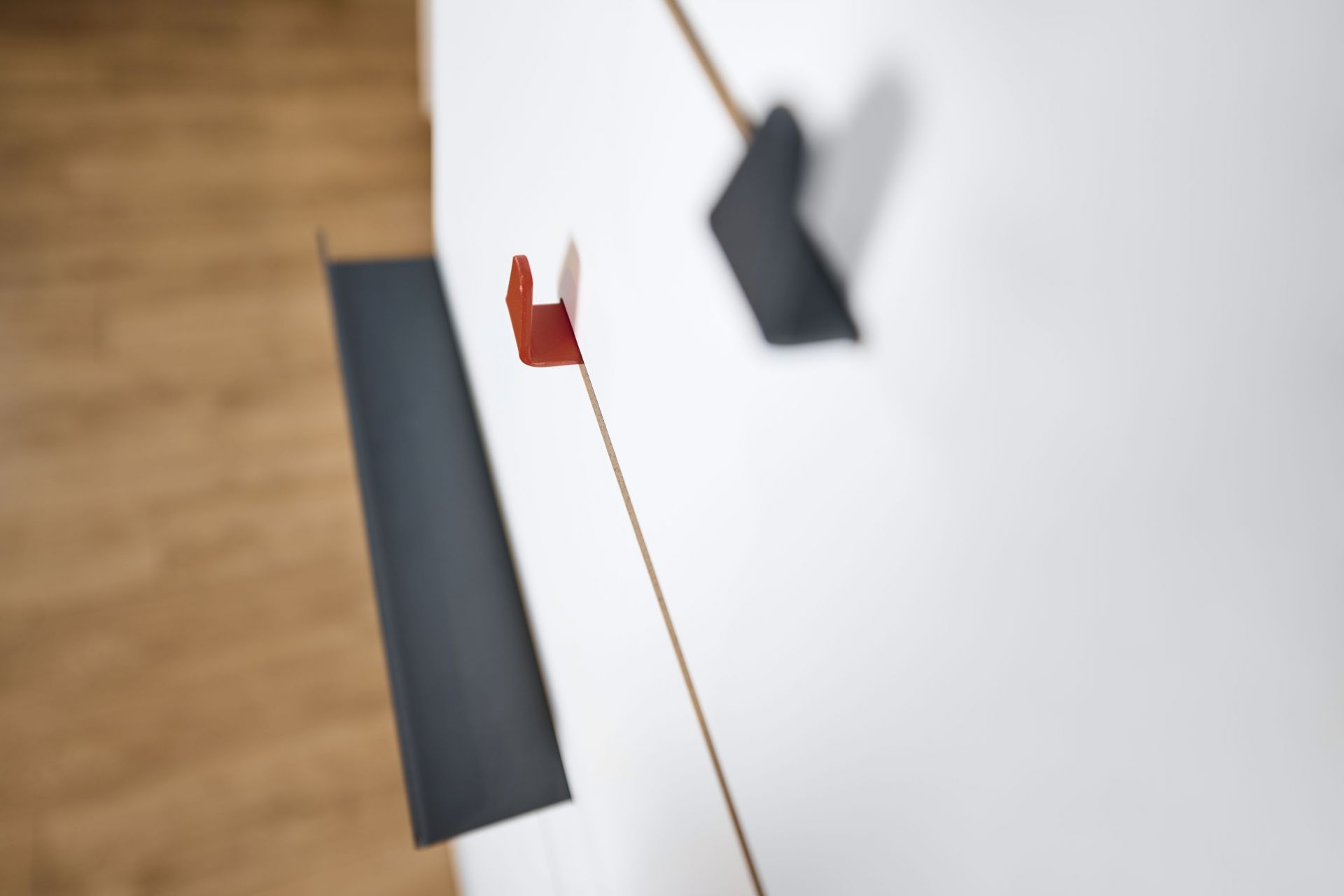 Drei Tojo Angeber Haken in Rot und Grau an einer weißen Wand. Garderobenhaken Set.