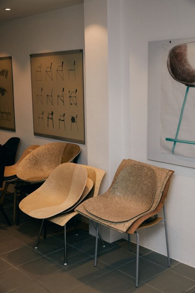 Mehrere Normann Copenhagen Mat Chair Steel Stühle mit Sitzschalen aus Kork auf grauem Fliesenboden.