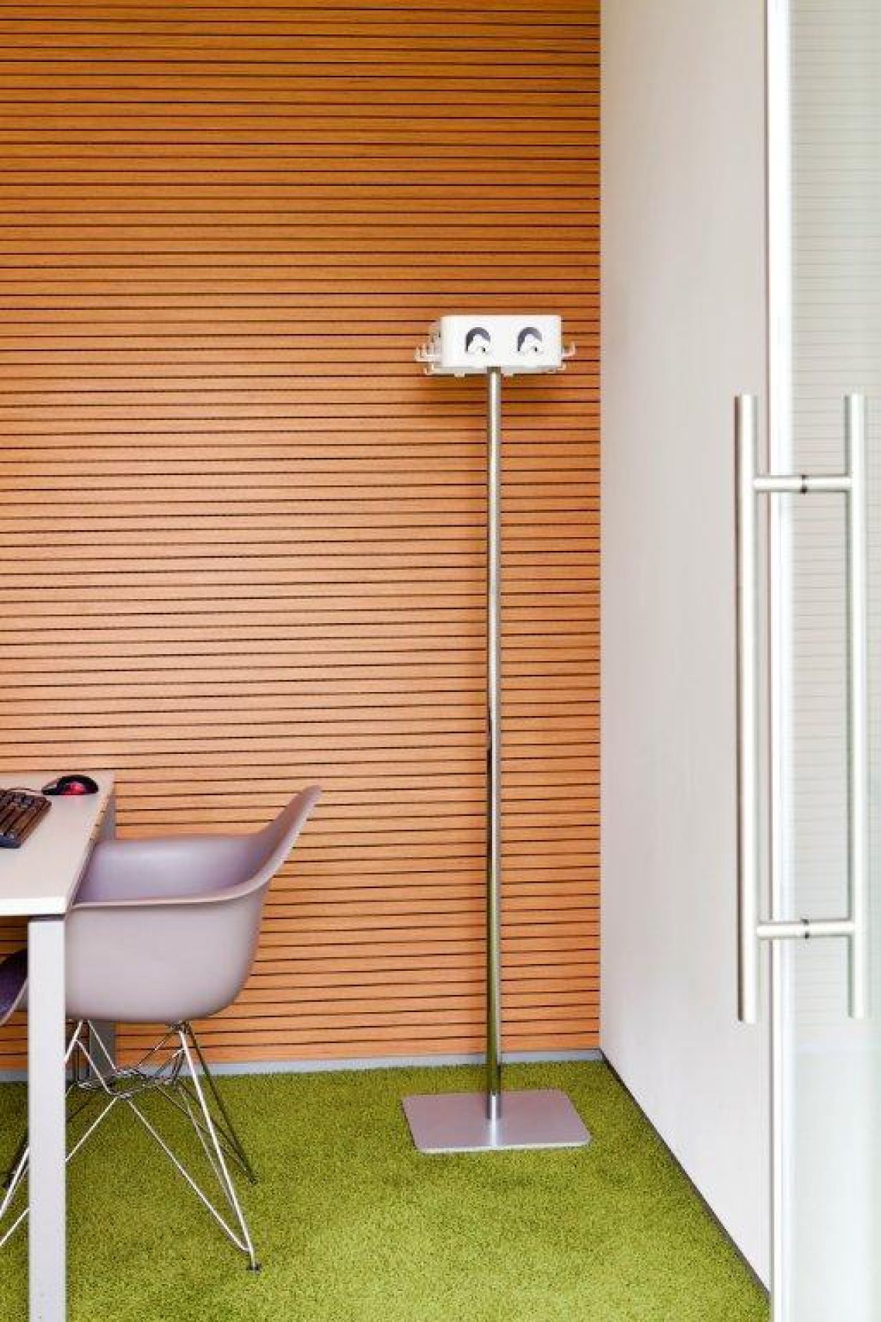 Steckdosen-Säule aus Metall im Büro mit Schreibtisch, Stuhl und Holzwand für flexible Stromversorgung.