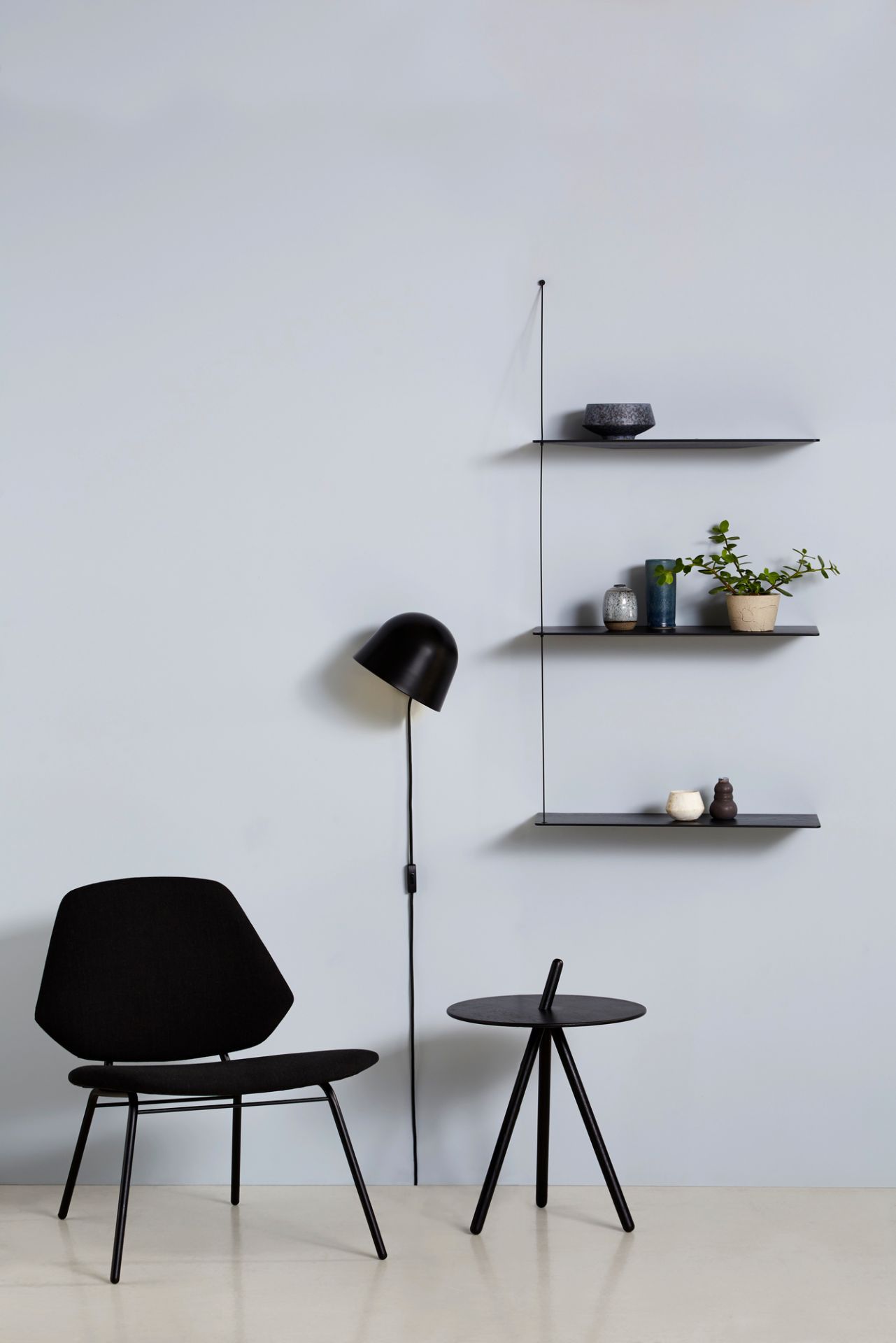 Kuppi Wandleuchte schwarz von Woud neben Stuhl und Regal mit Dekoration. Moderne Wandlampe.
