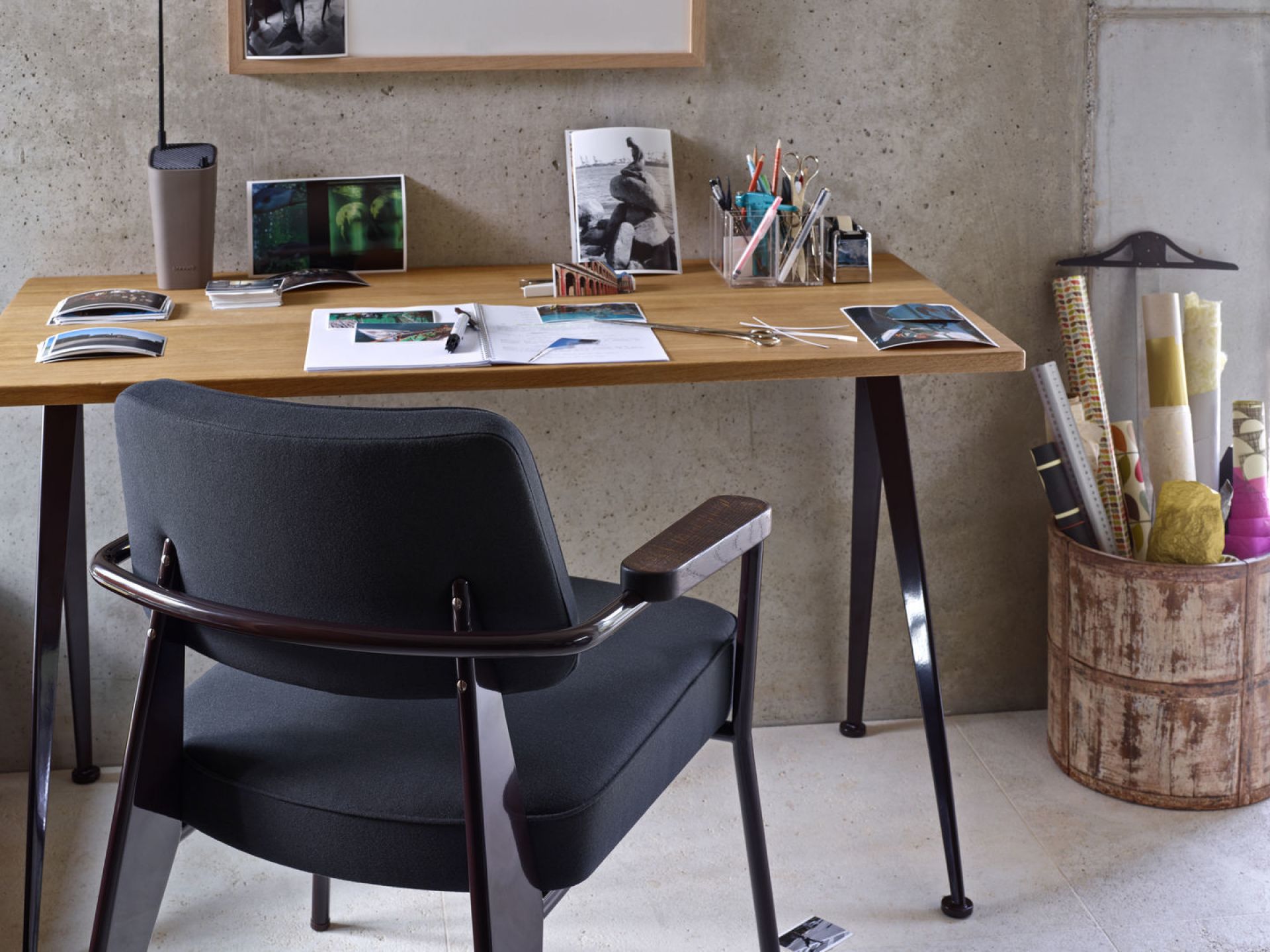 Vitra Fauteuil Direction Sessel in Schwarz vor Schreibtisch mit Büroartikeln und Betonwand.
