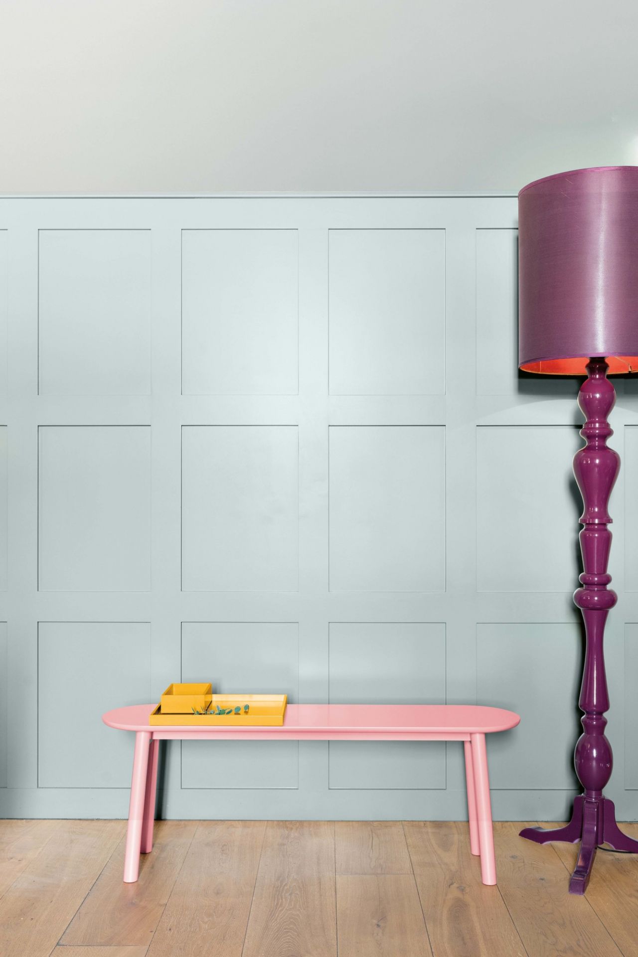 Rosa Schönbuch Mala Sitzbank (B 75 cm) mit gelben Tabletts und lila Stehlampe vor hellblauer Wand.
