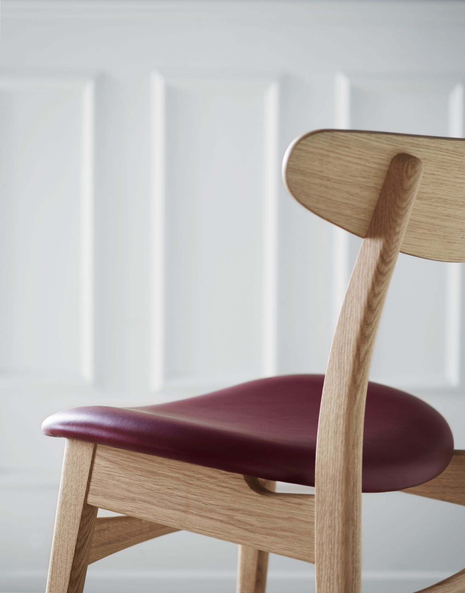 CH30P Stuhl von Carl Hansen: Detailaufnahme des Holzrahmens und des bordeauxroten, gepolsterten Ledersitzes.