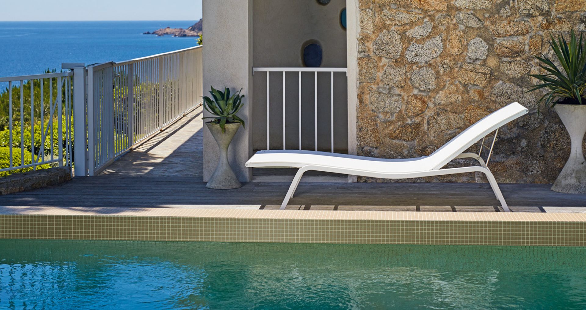 Weiße Alizé Sonnenliege von Fermob am Pool mit Meerblick für entspannte Stunden im Garten.
