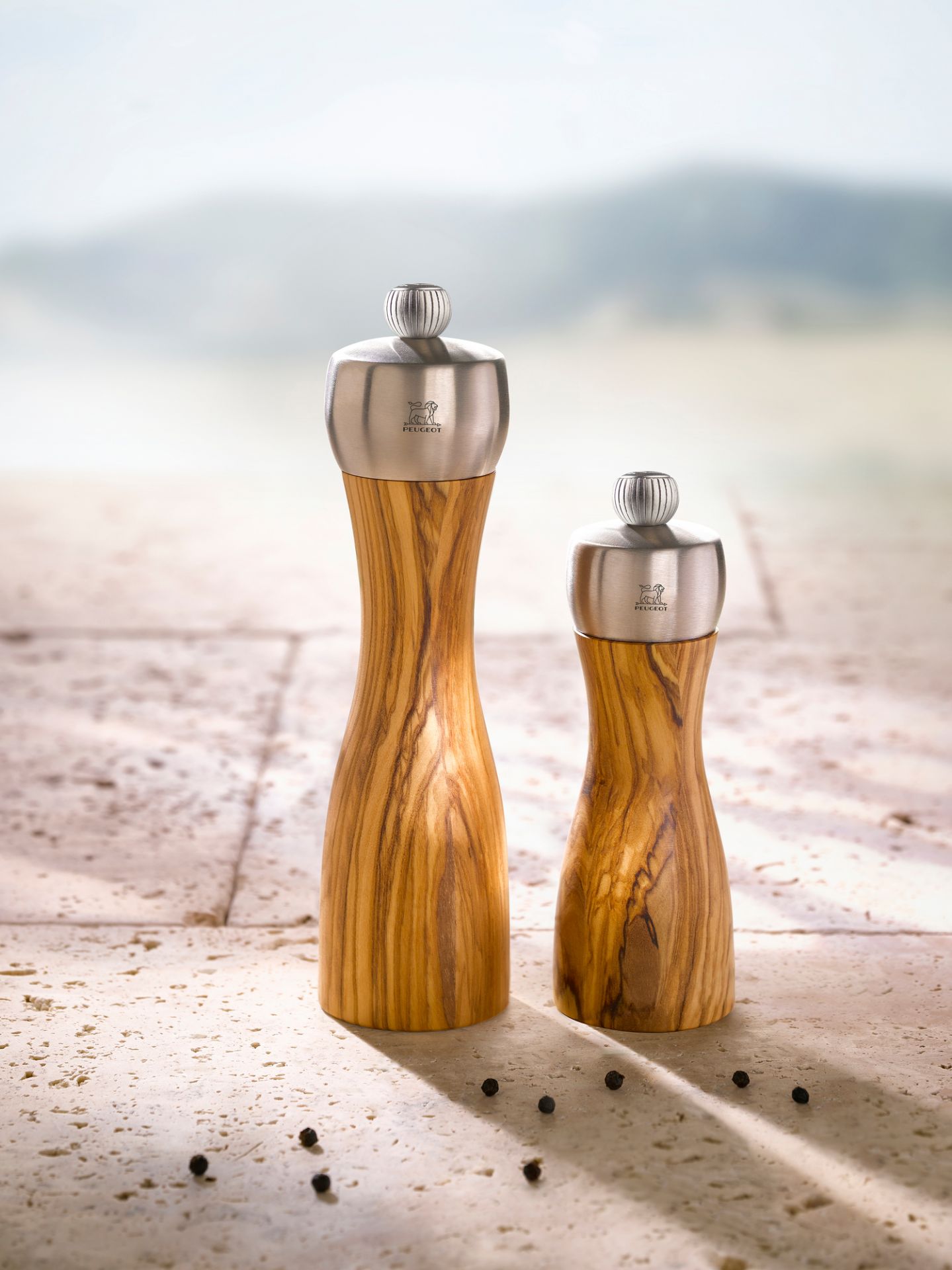 Zwei Peugeot Fidji Salzmühlen aus Olivenholz mit Edelstahlkopf, 20cm, auf Steintisch.