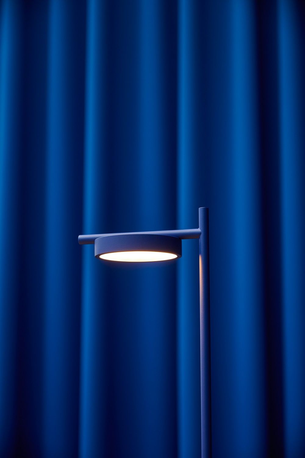 Igram Akku Tischleuchte von Grupa, blau, mit warmweißem Licht vor blauem Vorhang.