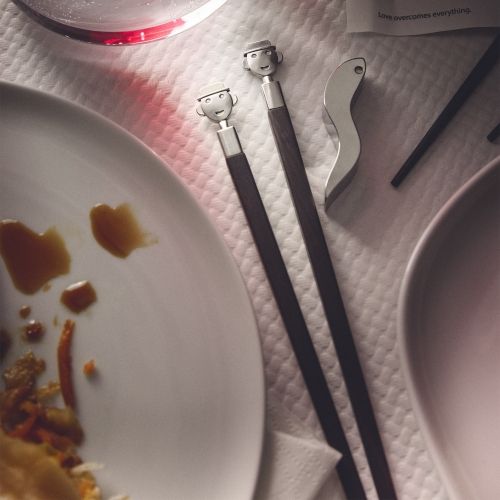 Alessi Anna Stick Essstäbchen Set AM44SET2 mit lustigen Gesichtern auf einem gedeckten Esstisch.