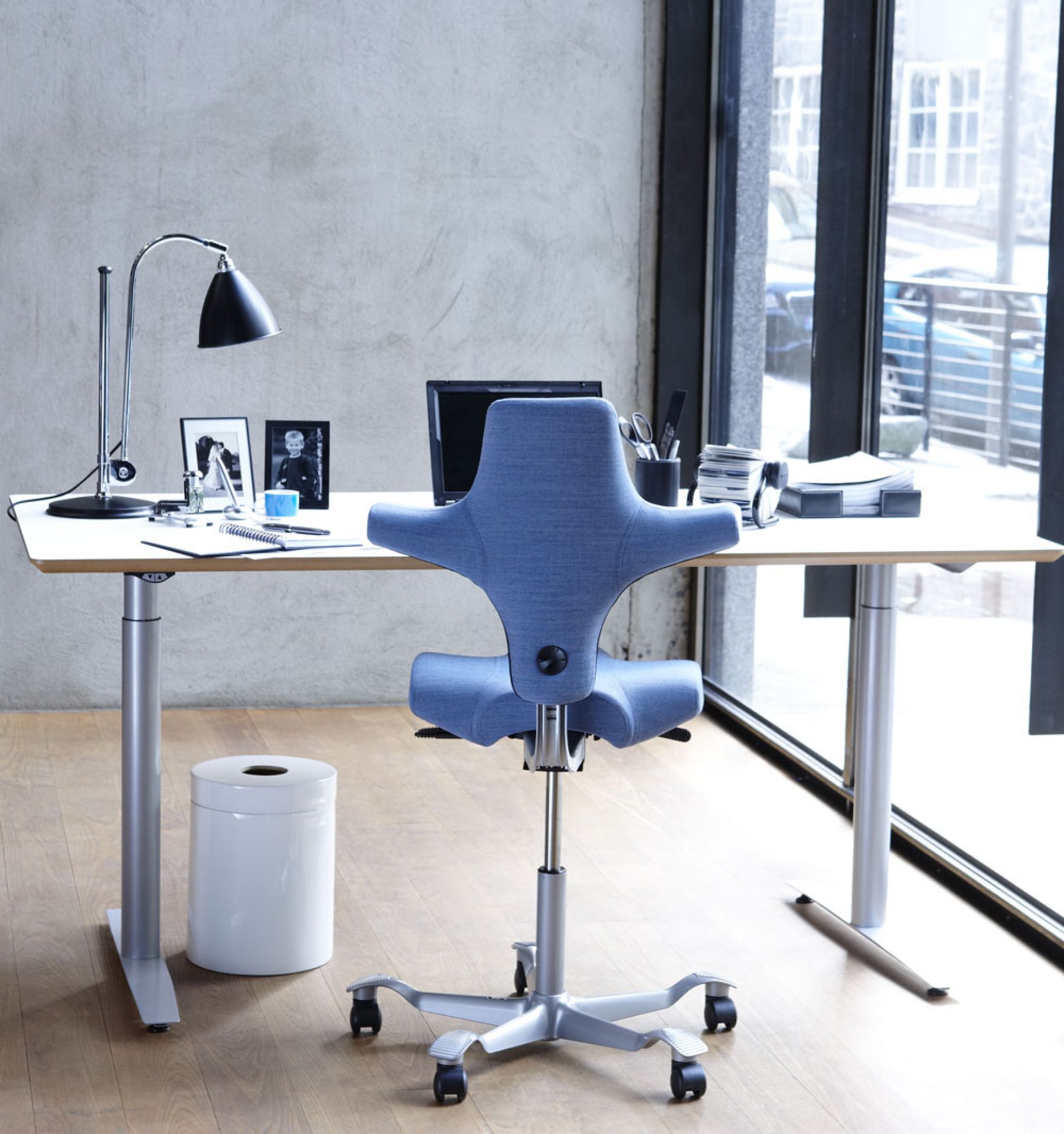Blauer HAG Capisco Bürostuhl vor Schreibtisch mit Lampe und Büromaterial. Ergonomischer Arbeitsstuhl.