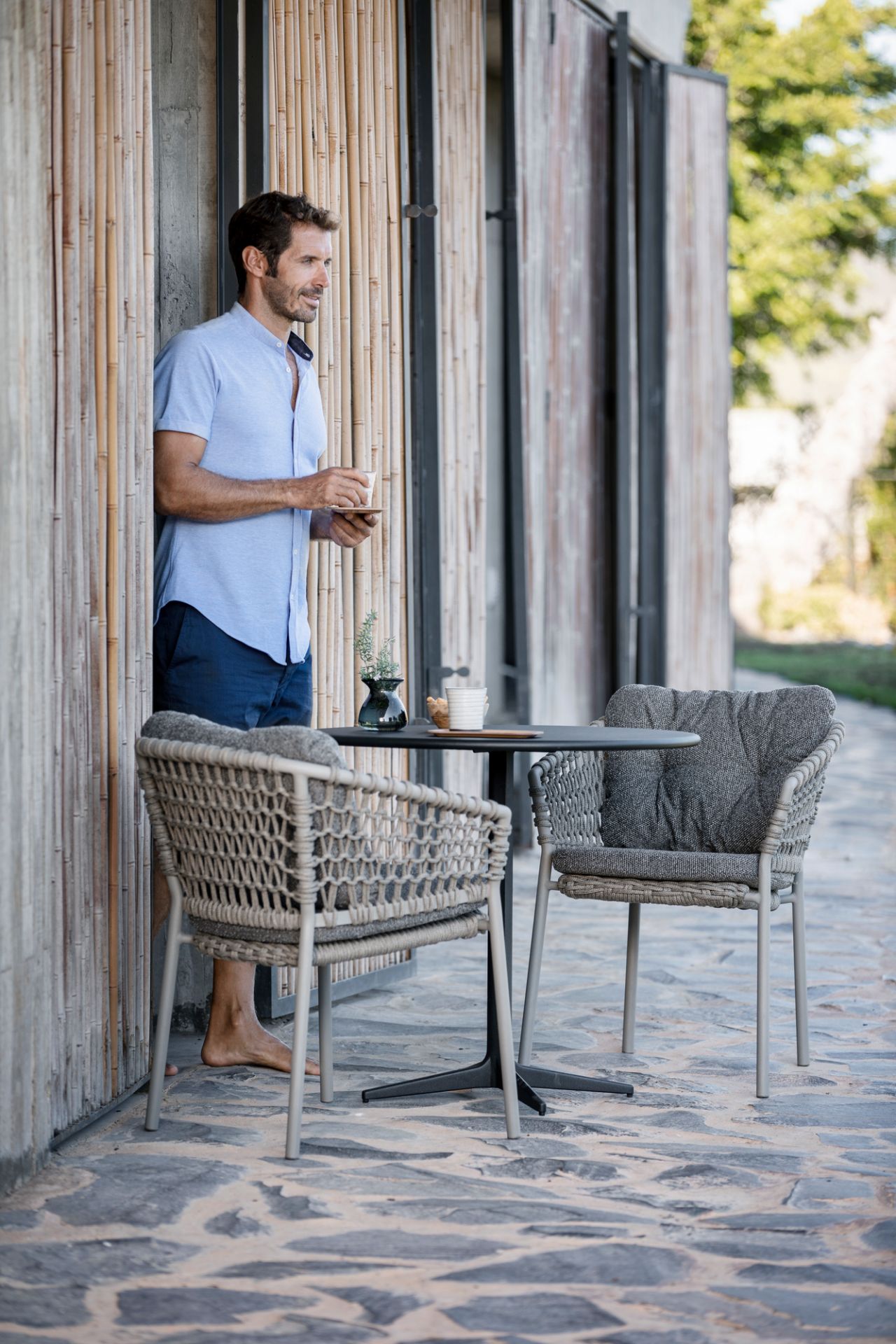Ocean Sessel von Cane-Line: Geflochtene Outdoor-Sessel mit Kissen und Tisch auf einer Terrasse.