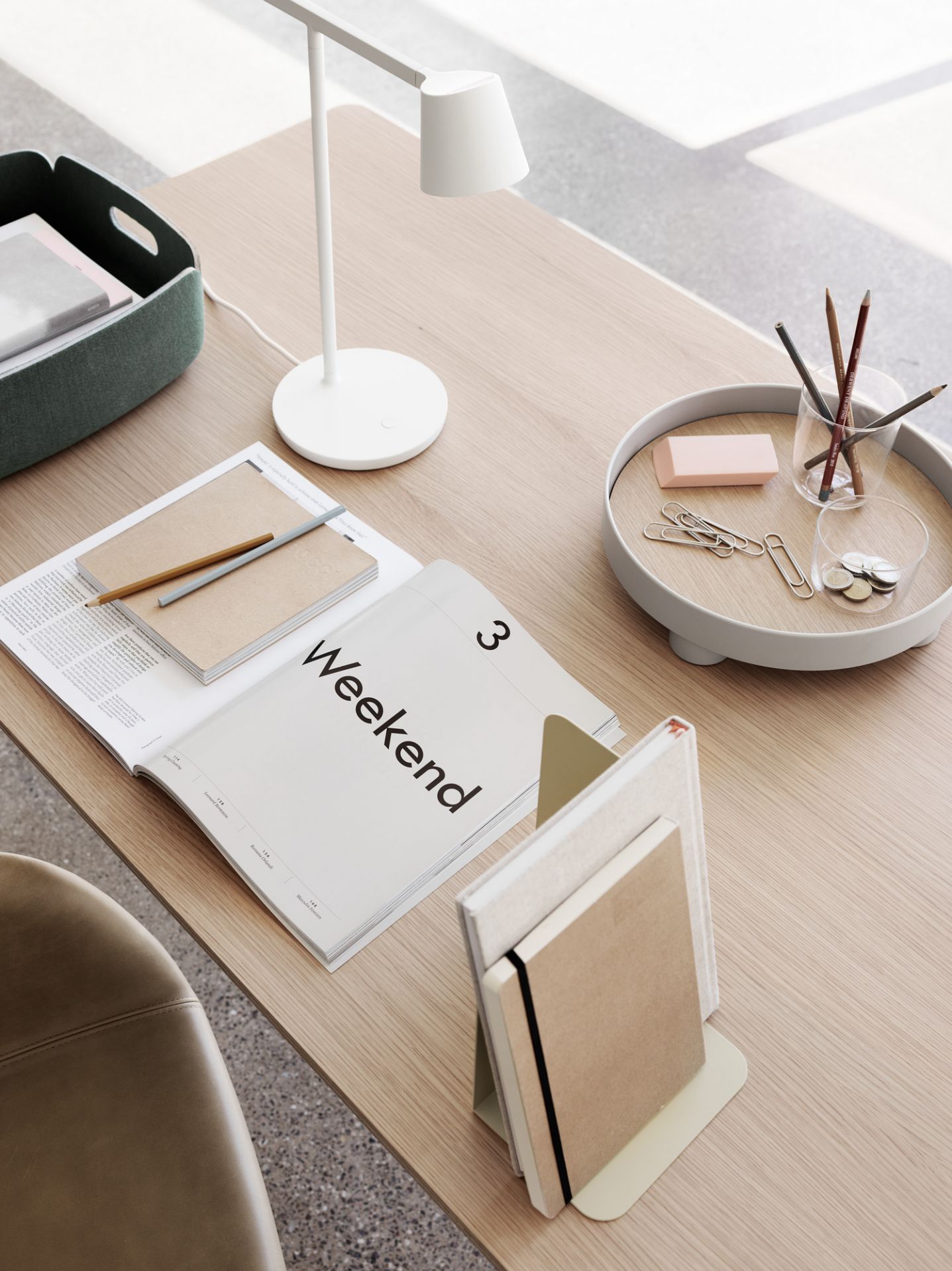 Detailaufnahme eines hellen Base Table Tisches von Muuto mit Schreibtischlampe, Notizbüchern und Büroaccessoires.