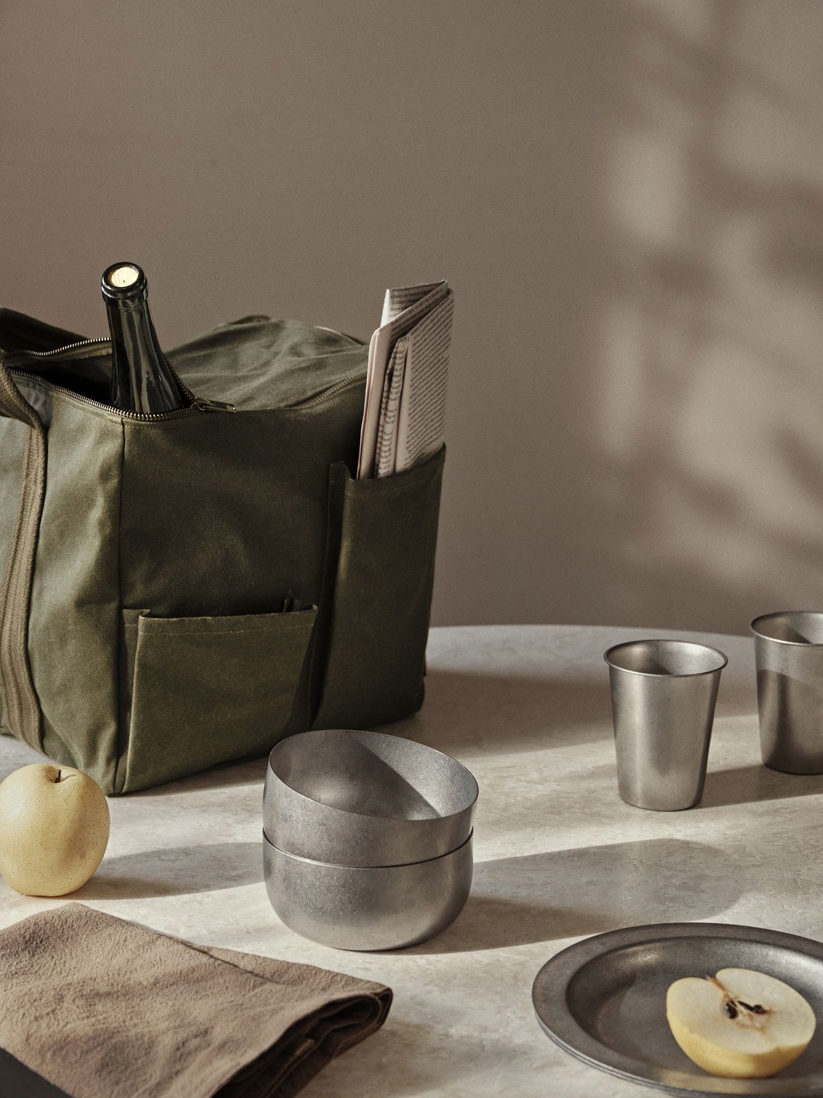 Ferm Living Tumbled Cup Campingtasse mit Picknicktasche, Flasche, Zeitung, Obst und Geschirr auf Tisch.