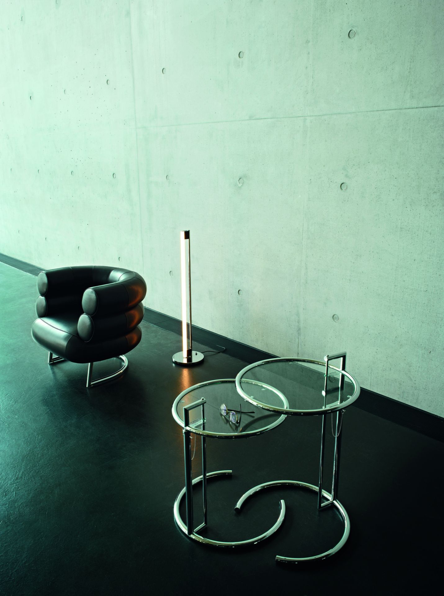 Moderner Adjustable Table E1027 Beistelltisch ClassiCon mit Glasplatte und verchromtem Gestell neben Sessel und Lampe.