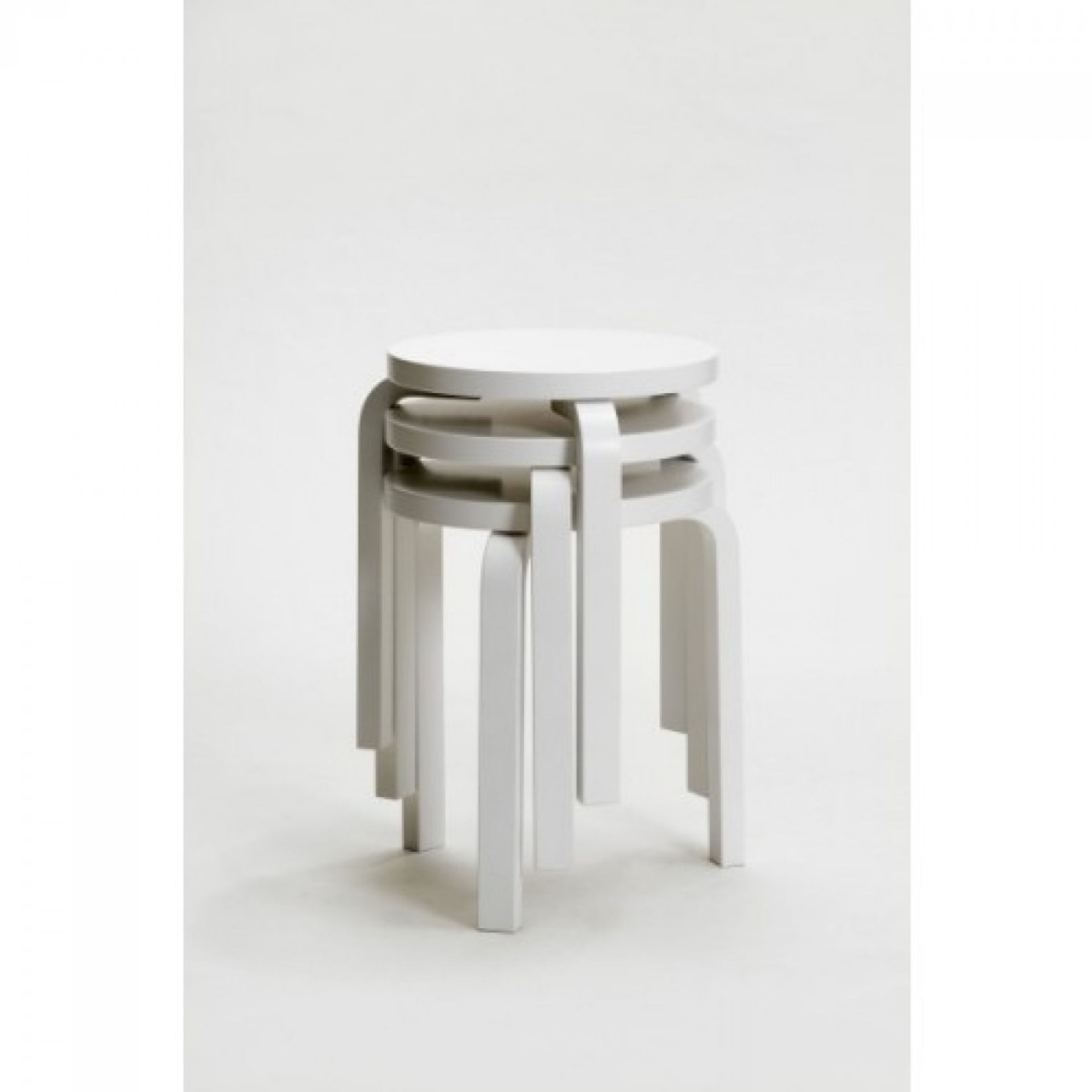 Drei weiße Artek Hocker 60 gestapelt, ikonisches Design, vielseitig einsetzbar und platzsparend, für modernes Wohnen.