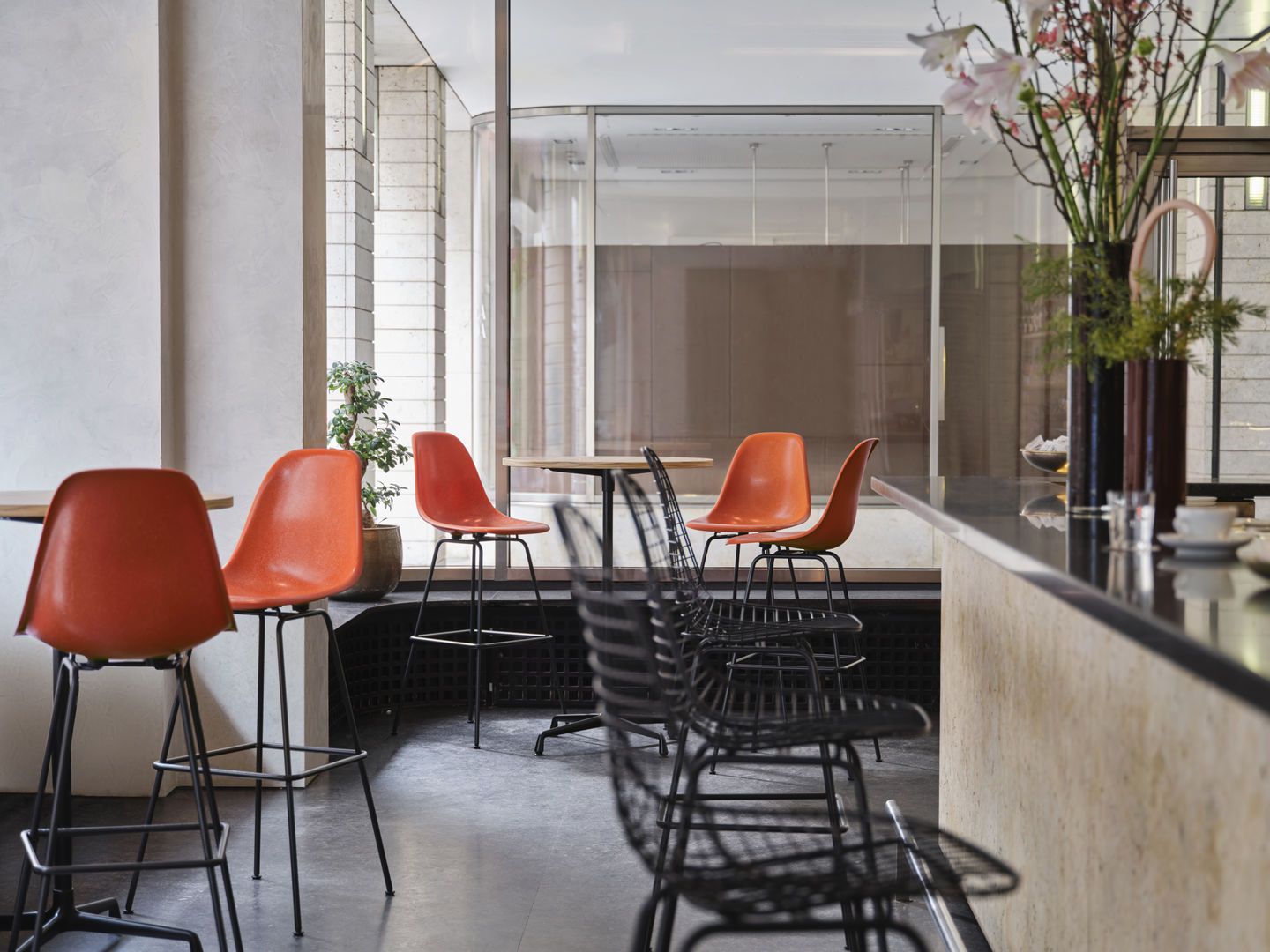 Eames Wire Bar Stool Barhocker High von Vitra, orangefarbene Sitzschale und filigranes Drahtgestell in Bar-Atmosphäre.