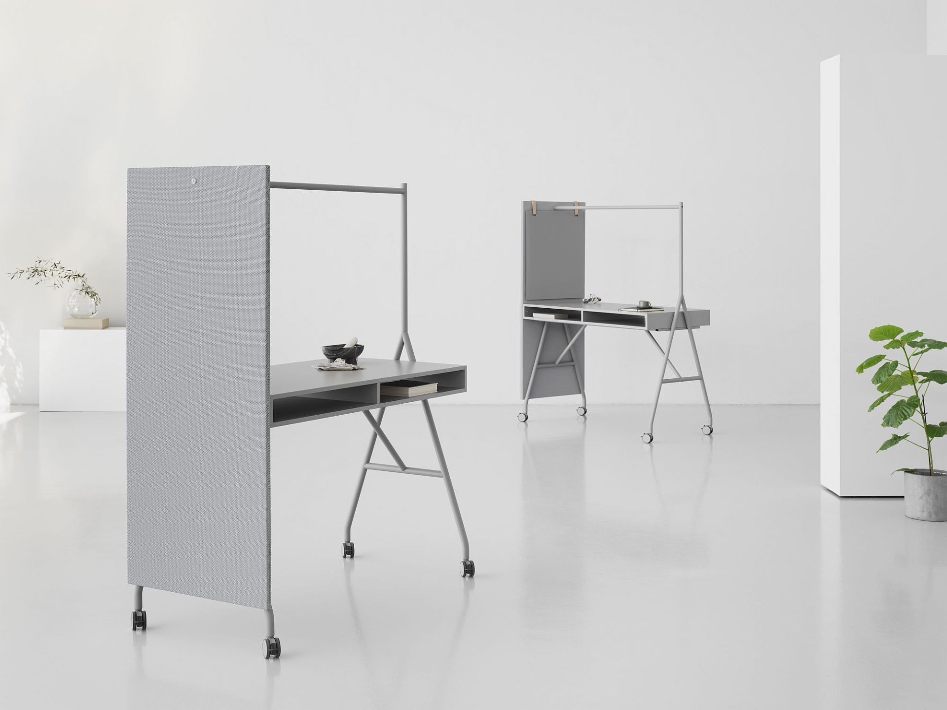Zwei graue Hangout High Desk Stehtische von Mizetto mit Rollen und Trennwand in einem hellen Raum.
