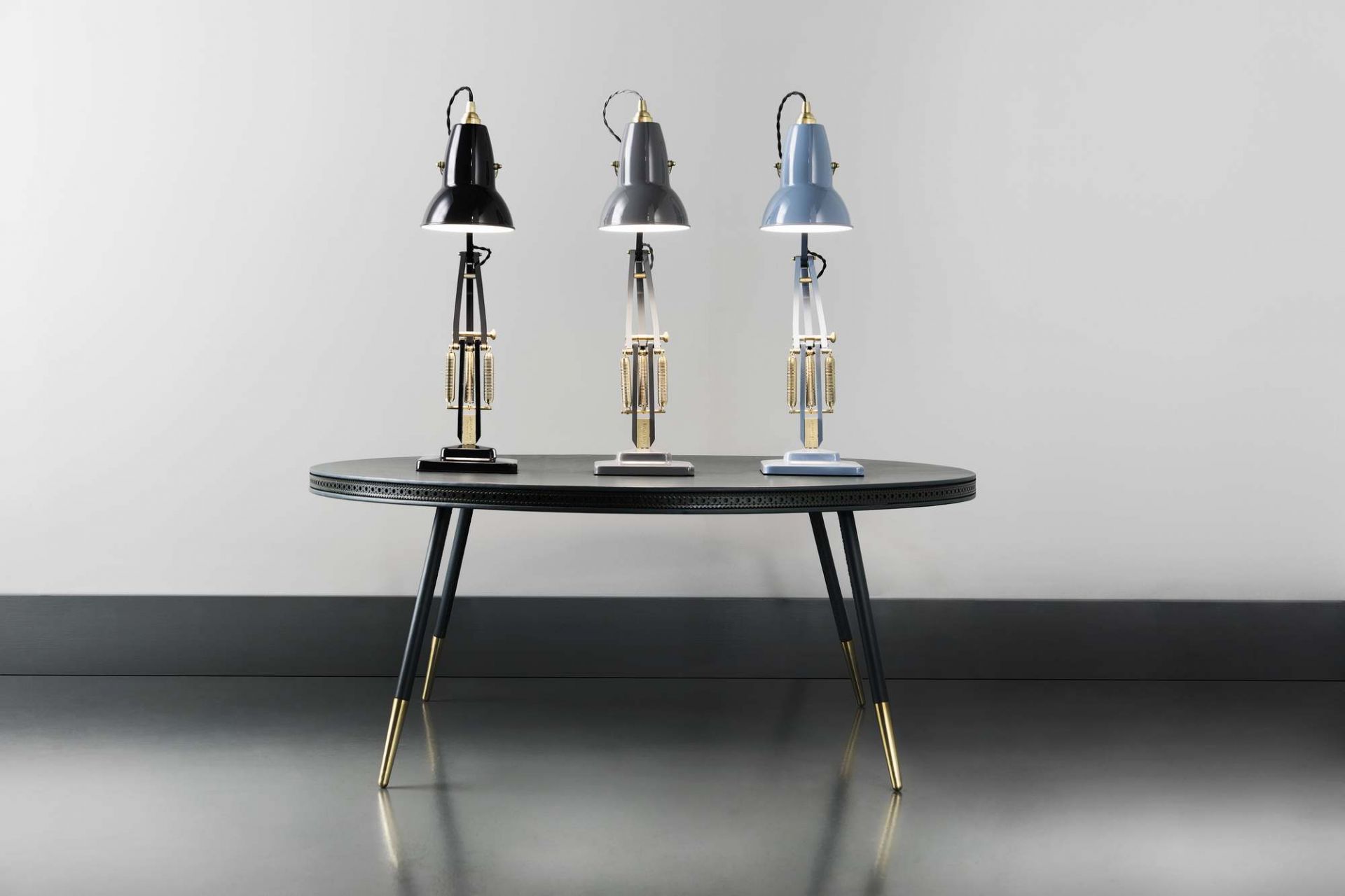 Drei Anglepoise Original 1227 Brass Tischleuchten in Schwarz, Grau und Blau auf einem Tisch.