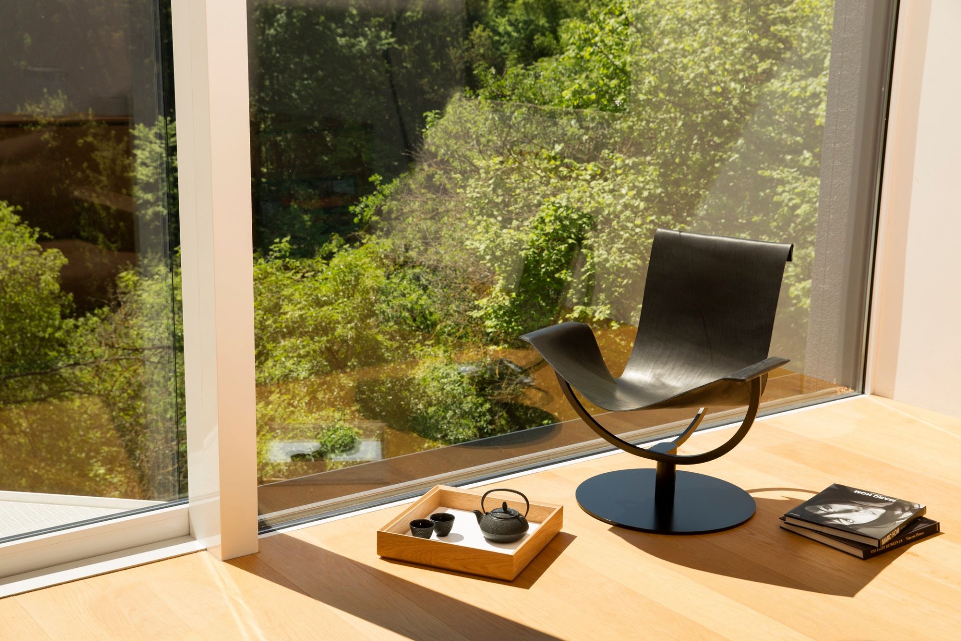 Arch Chair Sessel Favius aus schwarzem Leder vor Fenster mit Teegeschirr und Büchern.