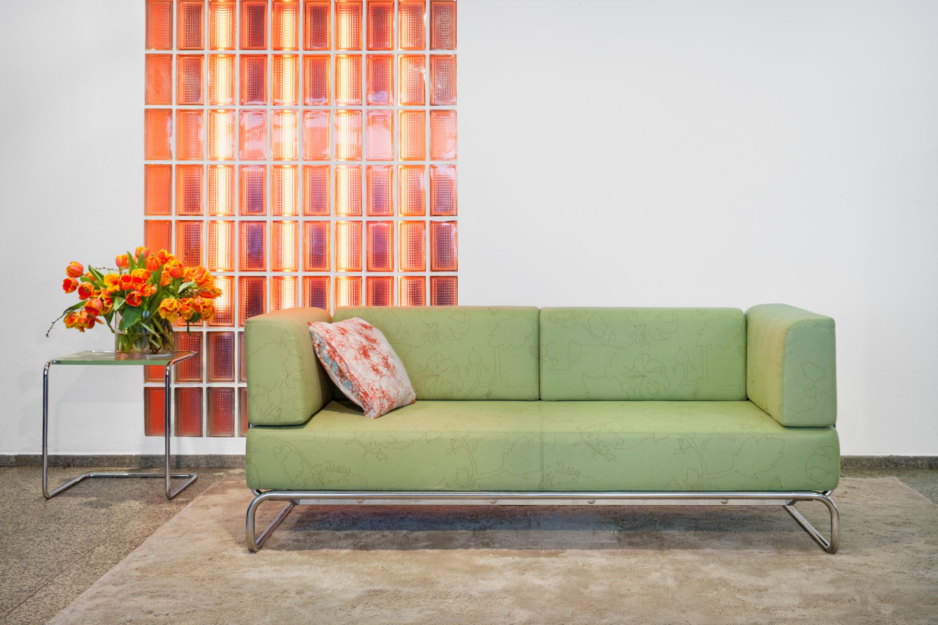 B97 a Thonet Beistelltisch aus Stahlrohr neben einem grünen Sofa und einem Blumenstrauß.
