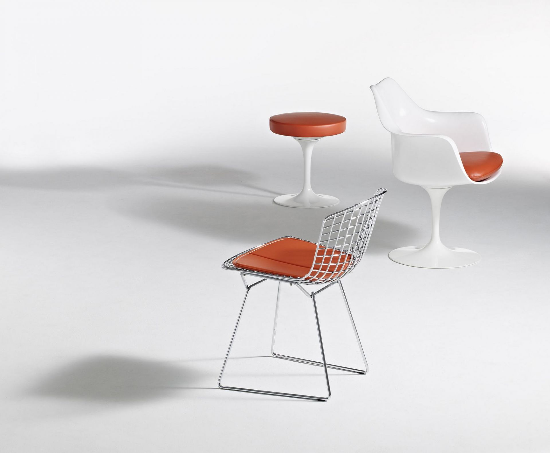 Knoll International Tulpen Armlehnenstuhl drehbar und weitere Designermöbel mit orangefarbenen Sitzkissen auf weißem Hintergrund.