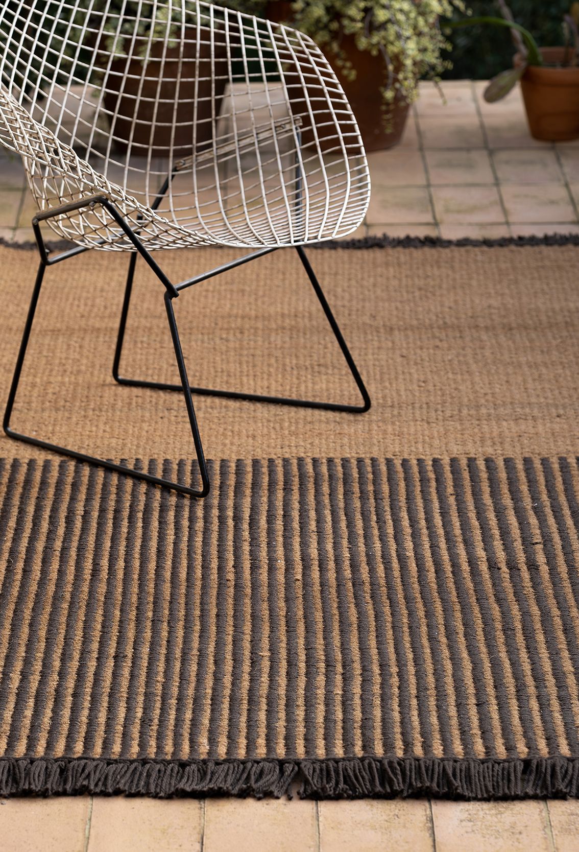 Nanimarquina Garden Outdoor Teppich mit Streifenmuster und Fransen, kombiniert mit modernem Drahtstuhl auf Terrasse.